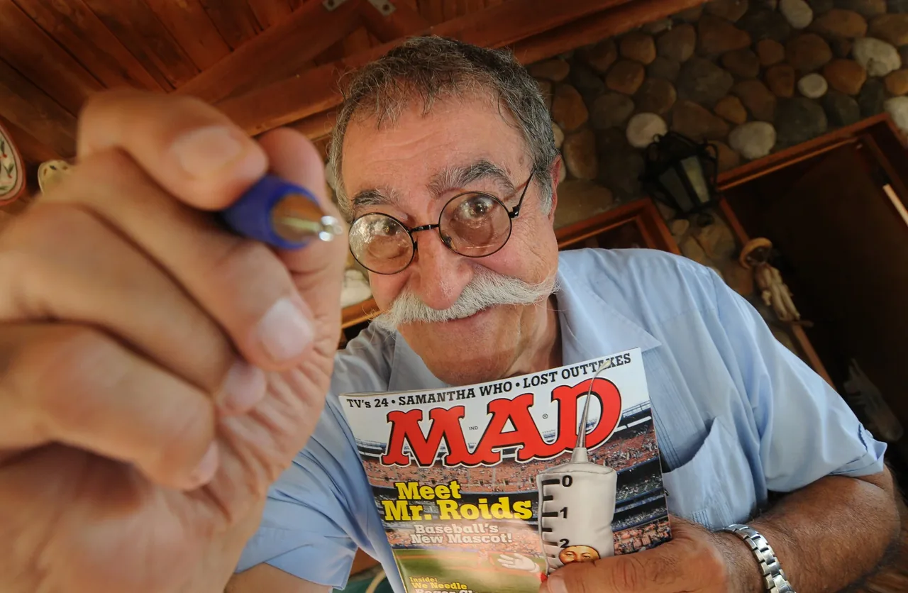 A cartoonist holding up a pen and a copy of MAD Magazine