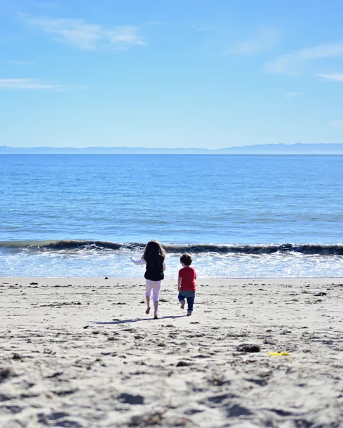 Two children running toward the ocean across a sandy beach