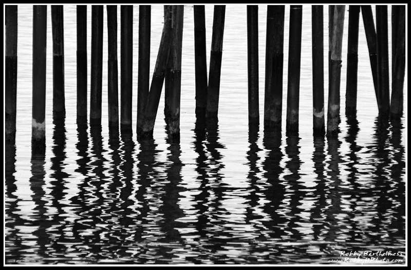 Pier pilings reflected in rippling water, in black and white