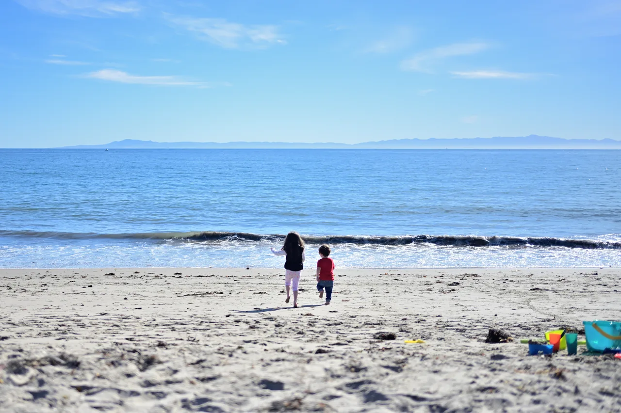 Two children running toward the ocean across a sandy beach