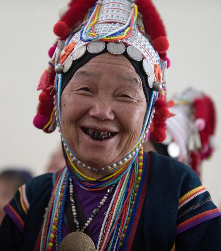 An older Akha woman in a beaded headdress laughing at a wedding, northern Thailand