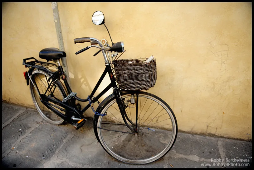 A black bicycle with a wicker basket against a yellow wall
