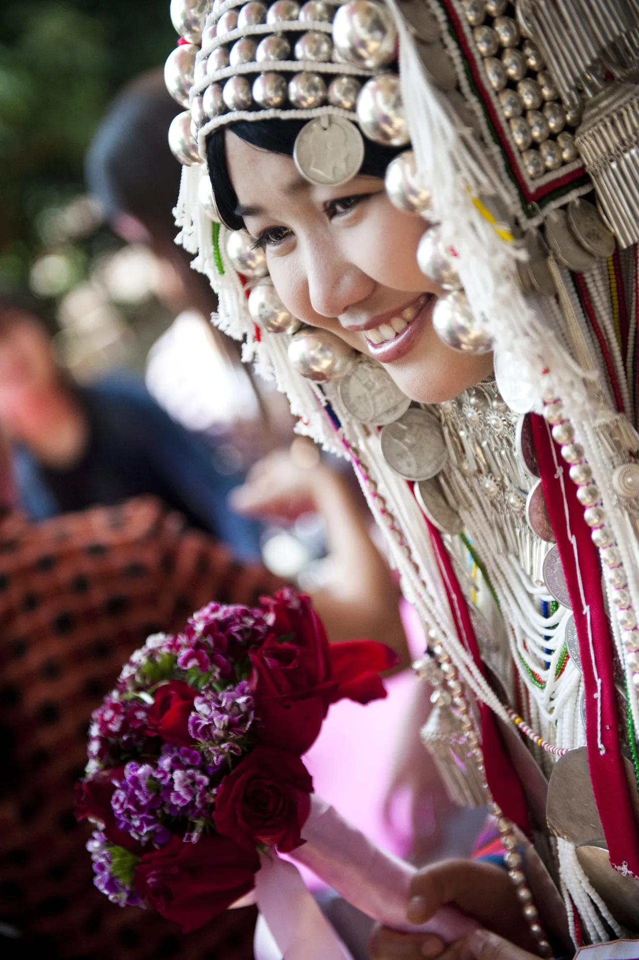 A smiling woman in a silver-beaded headdress holding flowers, Chiang Rai, Thailand
